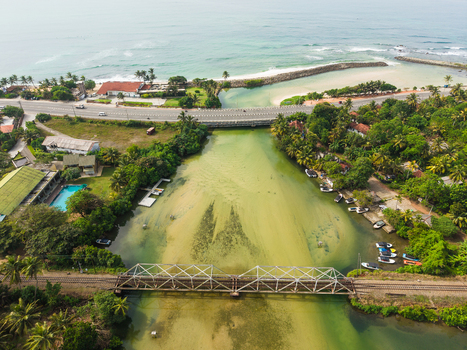Aerial view of the Koggala river mouth with a railway truss bridge coastal road and lush tropical greenery under a bright sky in Koggala Southern Province Sri Lanka. Aerial view of the Koggala river mouth with a railway truss bridge coastal road and lush tropical greenery under a bright sky in Koggala Southern Province Sri Lanka.