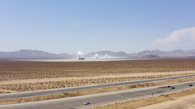 Aerial view of a large concentrated solar power plant with thousands of mirrors and central solar towers in a vast desert landscape with a highway in the foreground United States.