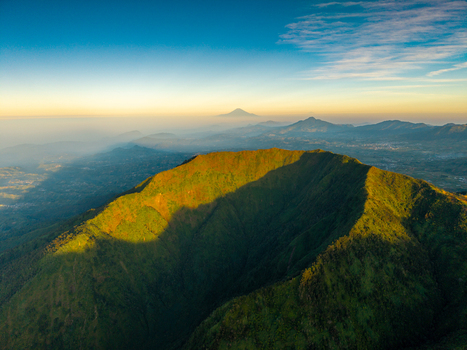 Aerial view of the lush green slopes of Mount Bismo at sunrise with golden light illuminating the volcanic landscape in Kecamatan Kejajar Jawa Tengah Indonesia.