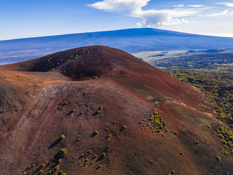 Aerial view of the red volcanic cinder cone of Mauna Kea with sparse vegetation under a blue sky in Hawaii County Hawaii United States.