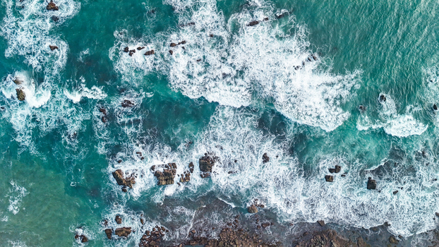 Aerial view of turquoise ocean waves crashing against dark rocks along the coastline of Indonesia. Aerial view of turquoise ocean waves crashing against dark rocks along the coastline of Indonesia.