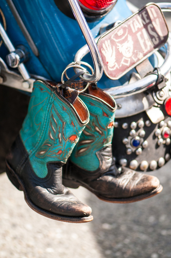 View of a pair of turquoise and black cowboy boots hanging from a motorcycle with a decorative license plate in Canada. View of a pair of turquoise and black cowboy boots hanging from a motorcycle with a decorative license plate in Canada.