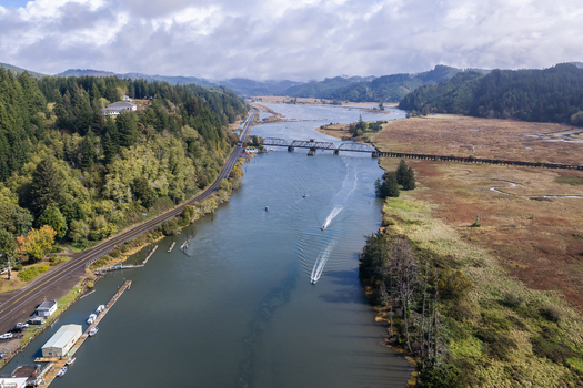 Aerial view of the Coos Bay Rail Line crossing the Siuslaw River near Florence Oregon with salmon fishing boats wetlands and a coastal transport corridor.