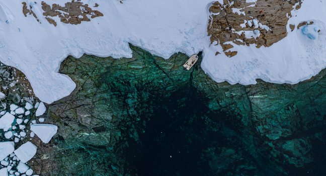 Aerial view of a small boat moored at the edge of a snowy shoreline with turquoise arctic waters and scattered ice floes Tasiilaq Sermersooq Municipality Greenland. Aerial view of a small boat moored at the edge of a snowy shoreline with turquoise arctic waters and scattered ice floes Tasiilaq Sermersooq Municipality Greenland.