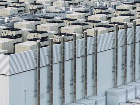 Aerial view of a large data center facility featuring numerous industrial cooling units ventilation fans and tall metallic exhaust pipes on the roof in the United Kingdom.