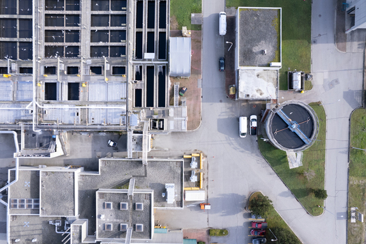 Aerial view of the Waste Water Treatment plant featuring rectangular sedimentation tanks a circular clarifier industrial buildings and service vehicles in Richmond British Columbia Canada. Aerial view of the Waste Water Treatment plant featuring rectangular sedimentation tanks a circular clarifier industrial buildings and service vehicles in Richmond British Columbia Canada.