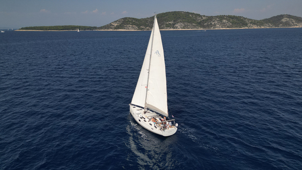 Croatia 22 August 2023 Aerial view of a white sailboat with people on deck navigating the blue Adriatic Sea near the islands of Hvar. Croatia 22 August 2023 Aerial view of a white sailboat with people on deck navigating the blue Adriatic Sea near the islands of Hvar.