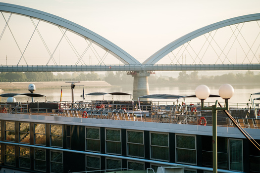 View of the Zezelj Bridge spanning the Danube river with a river cruise ship docked in the foreground under soft morning light in Novi Sad Vojvodina Serbia. View of the Zezelj Bridge spanning the Danube river with a river cruise ship docked in the foreground under soft morning light in Novi Sad Vojvodina Serbia.