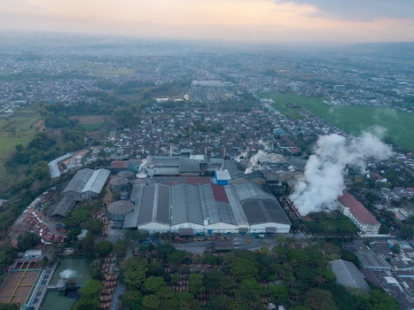 Aerial view of a large sugar factory complex with smoking chimneys industrial rooftops and surrounding residential neighborhoods in Malang East Java Indonesia.