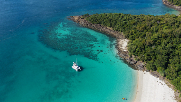 Aerial view of a catamaran anchored in the turquoise waters of Whitehaven Beach with white sand and lush tropical vegetation along the coastline in Whitsundays Queensland Australia.