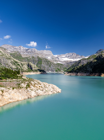 View of the turquoise waters of Lac d Emosson surrounded by rocky mountains and snow capped peaks under a clear blue sky in Le Chatelard Fribourg Switzerland. View of the turquoise waters of Lac d Emosson surrounded by rocky mountains and snow capped peaks under a clear blue sky in Le Chatelard Fribourg Switzerland.