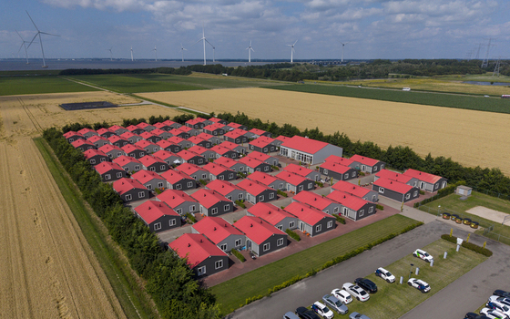 Aerial view of prefabricated housing for migrant and seasonal workers with rows of red roofed houses near agricultural fields and wind turbines in Swifterbant Flevoland Netherlands. Aerial view of prefabricated housing for migrant and seasonal workers with rows of red roofed houses near agricultural fields and wind turbines in Swifterbant Flevoland Netherlands.