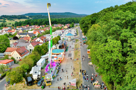 Forchheim Germany 25 July 2025 Aerial view of the Annafest fairground with a tall amusement ride carousel and people walking near the forest and residential houses. Forchheim Germany 25 July 2025 Aerial view of the Annafest fairground with a tall amusement ride carousel and people walking near the forest and residential houses.