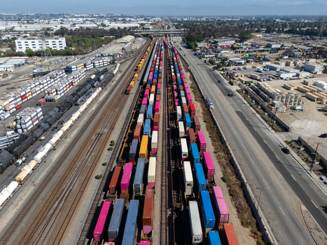Aerial view of a busy freight train yard filled with colorful shipping containers on multiple parallel tracks in Carson California United States.