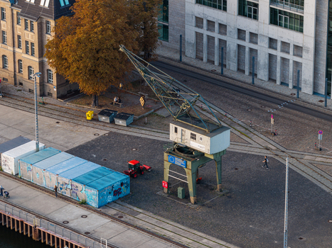 Aerial view of the historic crane at Spreespeicher Promenade with shipping containers a red tractor and a person walking along the waterfront in Berlin Berlin Germany. Aerial view of the historic crane at Spreespeicher Promenade with shipping containers a red tractor and a person walking along the waterfront in Berlin Berlin Germany.