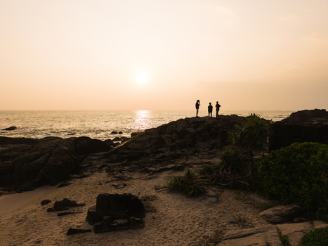 Aerial view of people standing on a rocky shoreline silhouetted against a golden sunset over the Indian Ocean in Galle Southern Province Sri Lanka.