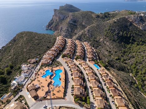 Aerial view of a residential complex with terraced houses swimming pools and lush hills overlooking the Mediterranean Sea in Moraira Valencian Community Spain.
