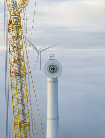 Netherlands 26 November 2025 Aerial view of a wind turbine nacelle with workers visible inside and a yellow crane rising above a thick layer of clouds. Netherlands 26 November 2025 Aerial view of a wind turbine nacelle with workers visible inside and a yellow crane rising above a thick layer of clouds.