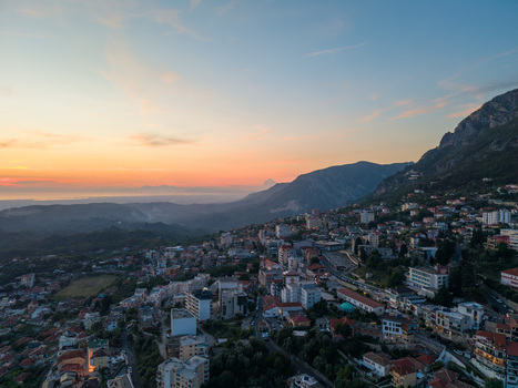 Aerial view of the hillside town of Kruje with residential buildings nestled against rugged mountains under an orange and blue sunset sky in Kruje Durres County Albania.