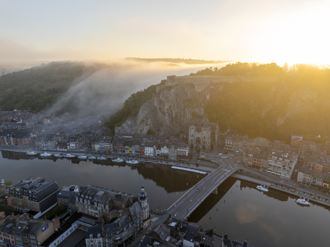 Aerial view of the Collegiate Church of Notre Dame de Dinant and the Citadel perched on the cliff above the Meuse River during a misty golden hour in Dinant Wallonia Belgium. Aerial view of the Collegiate Church of Notre Dame de Dinant and the Citadel perched on the cliff above the Meuse River during a misty golden hour in Dinant Wallonia Belgium.