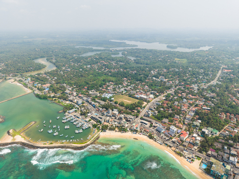 Aerial view of the coastal town of Hikkaduwa featuring a fishing harbour sandy beaches and turquoise ocean waters with lush greenery Hikkaduwa Southern Province Sri Lanka. Aerial view of the coastal town of Hikkaduwa featuring a fishing harbour sandy beaches and turquoise ocean waters with lush greenery Hikkaduwa Southern Province Sri Lanka.