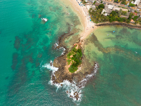 Aerial view of Parrot Rock island connected to the sandy beach by a narrow sandbar surrounded by turquoise ocean water and coral reefs in Mirissa Southern Province Sri Lanka. Aerial view of Parrot Rock island connected to the sandy beach by a narrow sandbar surrounded by turquoise ocean water and coral reefs in Mirissa Southern Province Sri Lanka.