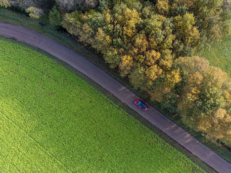 Aerial view of a lone red car traversing the road flanked by a vibrant green field and a forest with autumn hues Diever Drenthe Netherlands. Aerial view of a lone red car traversing the road flanked by a vibrant green field and a forest with autumn hues Diever Drenthe Netherlands.
