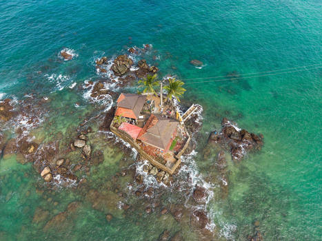 Aerial view of Seenigama Muhudu Dewalaya temple on a small rocky island surrounded by turquoise ocean water and palm trees in Peraliya Sri Lanka. Aerial view of Seenigama Muhudu Dewalaya temple on a small rocky island surrounded by turquoise ocean water and palm trees in Peraliya Sri Lanka.