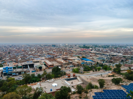 Aerial view of the urban landscape featuring residential and commercial buildings a solar panel array in the foreground and a hazy sky in Multan Punjab Pakistan.