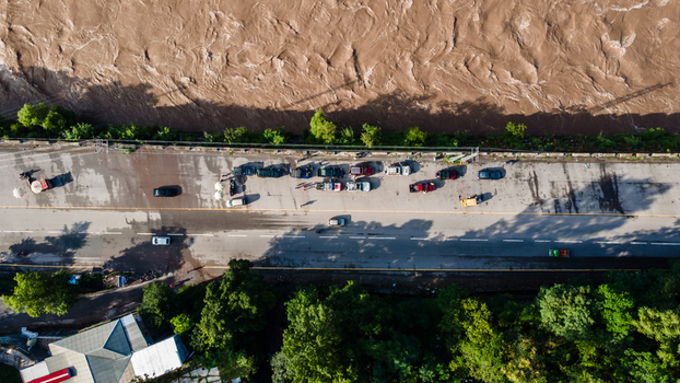 Aerial view of a muddy river flowing next to a road with parked cars and lush green trees in Muzaffarabad Azad Kashmir Pakistan. Aerial view of a muddy river flowing next to a road with parked cars and lush green trees in Muzaffarabad Azad Kashmir Pakistan.