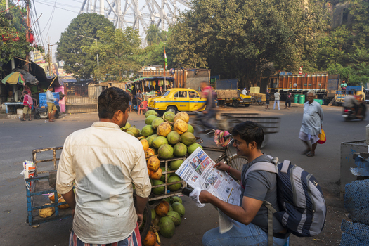 Kolkata India 05 December 2024 View of a bustling street scene near the Howrah Bridge with a coconut vendor and a reader immersed in a newspaper. Kolkata India 05 December 2024 View of a bustling street scene near the Howrah Bridge with a coconut vendor and a reader immersed in a newspaper.