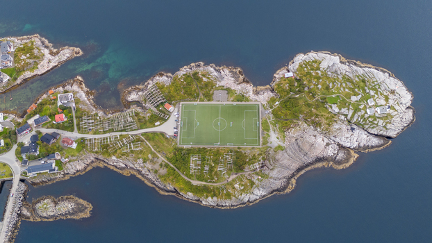 Aerial view of the iconic Henningsvaer football field on a rocky island surrounded by sea with wooden fish drying racks and rugged coastal terrain in Henningsvaer Nordland Norway. Aerial view of the iconic Henningsvaer football field on a rocky island surrounded by sea with wooden fish drying racks and rugged coastal terrain in Henningsvaer Nordland Norway.