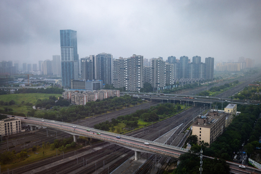 Aerial view of railway tracks and urban skyline near Chengdu East Railway Station with modern high rise buildings and a road overpass under a cloudy sky in Chengdu Sichuan China.