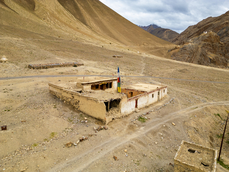 Aerial view of a traditional mud brick building with prayer flags in a vast arid mountain landscape in Zanskar Ladakh India.
