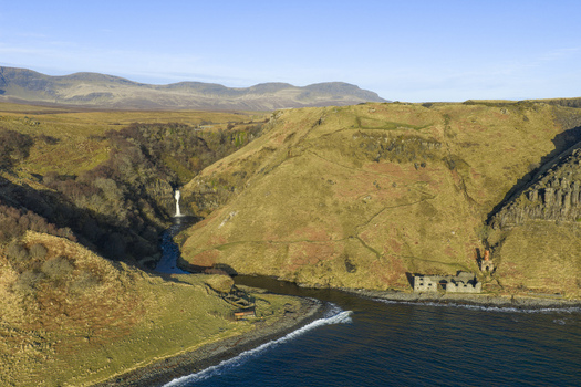 Aerial view of Lealt Falls cascading through a steep gorge towards the sea with historic ruins on the shore and rugged mountains in the distance Isle of Skye Scotland United Kingdom. Aerial view of Lealt Falls cascading through a steep gorge towards the sea with historic ruins on the shore and rugged mountains in the distance Isle of Skye Scotland United Kingdom.