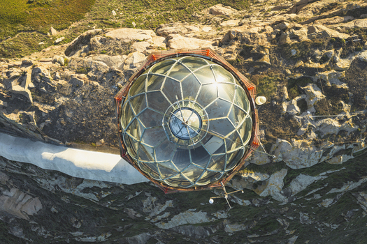 Aerial view of the glass dome of a lighthouse situated on a rocky cliffside in Galicia Spain.