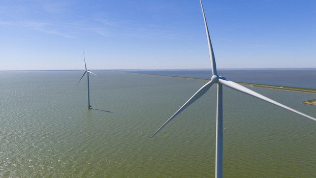 Aerial view of Windpark Fryslan offshore wind turbines standing in the IJsselmeer with a long dike in the background in Breezanddijk Friesland Netherlands. Aerial view of Windpark Fryslan offshore wind turbines standing in the IJsselmeer with a long dike in the background in Breezanddijk Friesland Netherlands.