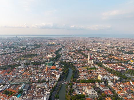 Surabaya Indonesia 28 August 2026 Aerial view of the sprawling urban landscape featuring dense residential rooftops a winding river and distant coastal views under a soft sky.