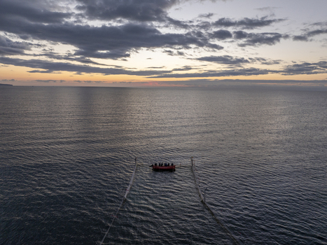 Aerial view of a small red boat with people on board floating in the calm sea at sunset near the historic town of Nessebar with a dramatic cloudy sky in Nessebar Burgas Bulgaria. Aerial view of a small red boat with people on board floating in the calm sea at sunset near the historic town of Nessebar with a dramatic cloudy sky in Nessebar Burgas Bulgaria.