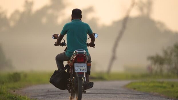 View of a man riding a motorcycle on a rural road Bangladesh.