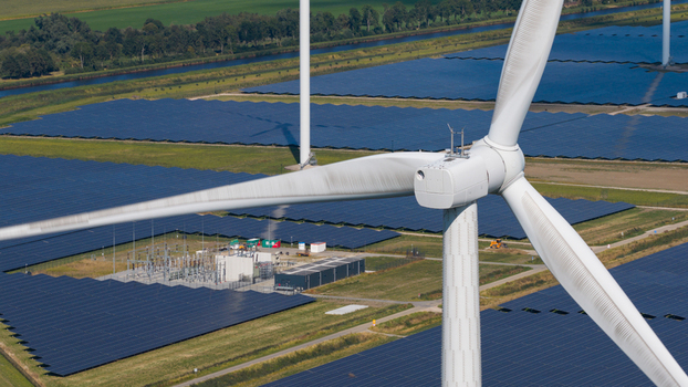 Aerial view of Zonnepark Eekerpolder featuring solar panels and a wind turbine set amidst green fields and power infrastructure in Scheemda Groningen Netherlands. Aerial view of Zonnepark Eekerpolder featuring solar panels and a wind turbine set amidst green fields and power infrastructure in Scheemda Groningen Netherlands.