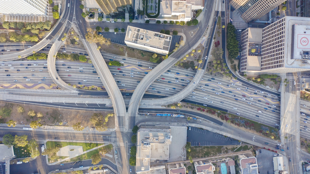 Aerial view of a complex multi level highway interchange with heavy traffic flow surrounded by urban skyscrapers and greenery in the city center. Los Angeles California United States.
