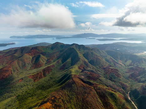 Aerial view of vibrant green and red mountains contrasting with the serene blue waters surrounding the islands Goro South Province New Caledonia. Aerial view of vibrant green and red mountains contrasting with the serene blue waters surrounding the islands Goro South Province New Caledonia.