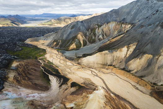 Aerial view of Landmannalaugar rhyolite mountains with a braided river valley and dark lava fields under a cloudy sky Rangarthing ytra Iceland. Aerial view of Landmannalaugar rhyolite mountains with a braided river valley and dark lava fields under a cloudy sky Rangarthing ytra Iceland.