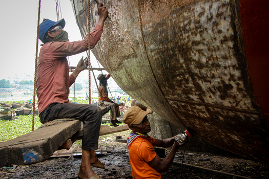 Keraniganj Bangladesh 03 November 2023 View of workers scraping and sanding the rusty hull of a large ship at Shipyard Dhaka on the banks of the Buriganga River.