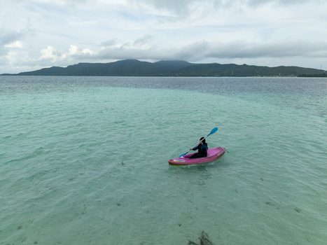 Aerial view of a lone kayaker paddling through the crystalline turquoise waters towards the distant mountainous island at Menjangan Kecil Island Karimunjawa Jawa Tengah Indonesia.