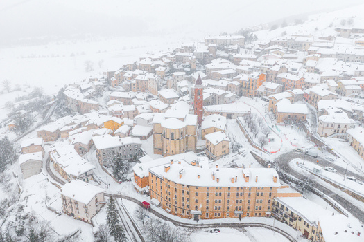 Aerial view of the historic town of Rivisondoli covered in a thick blanket of snow featuring traditional stone buildings a prominent bell tower and winding roads in Rivisondoli Abruzzo Italy.