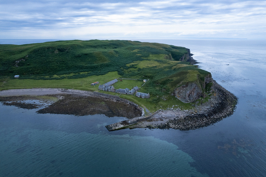 Aerial view of Sanda Island near the Mull of Kintyre featuring green hills historic stone buildings and a rocky coastline in Argyll and Bute Scotland United Kingdom. Aerial view of Sanda Island near the Mull of Kintyre featuring green hills historic stone buildings and a rocky coastline in Argyll and Bute Scotland United Kingdom.