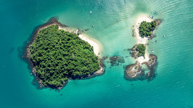 Aerial view of Ilha de Cataguas featuring lush tropical vegetation white sandy beaches and turquoise waters with small boats in Angra dos Reis State of Rio de Janeiro Brazil.