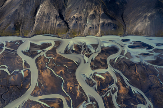 Aerial view of braided glacial river flowing through dark volcanic landscape in the Iceland Highlands Iceland. Aerial view of braided glacial river flowing through dark volcanic landscape in the Iceland Highlands Iceland.